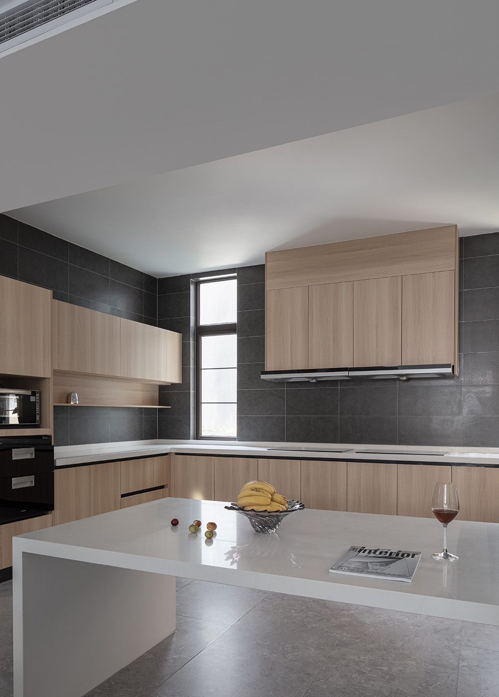 Warm minimalist kitchen with a black tile backsplash, wood cabinetry, and clean countertops.