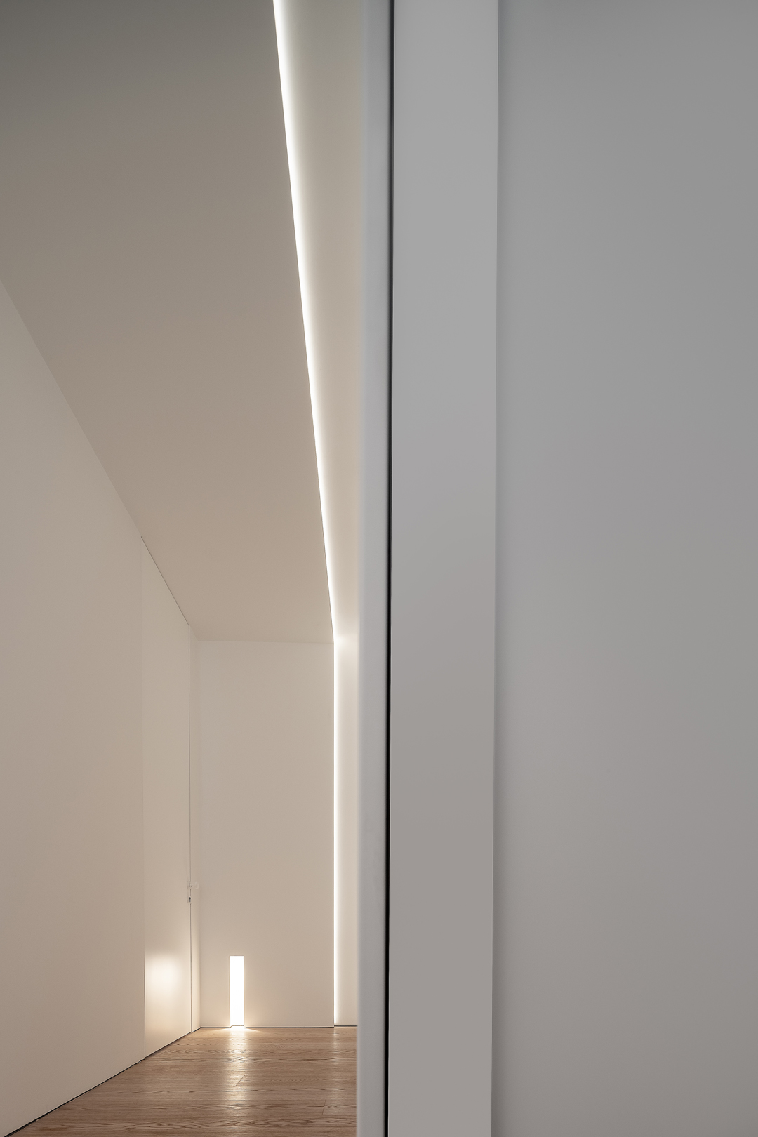 Minimalist apartment interior with recessed linear ceiling lighting, smooth white walls, and light wood flooring.