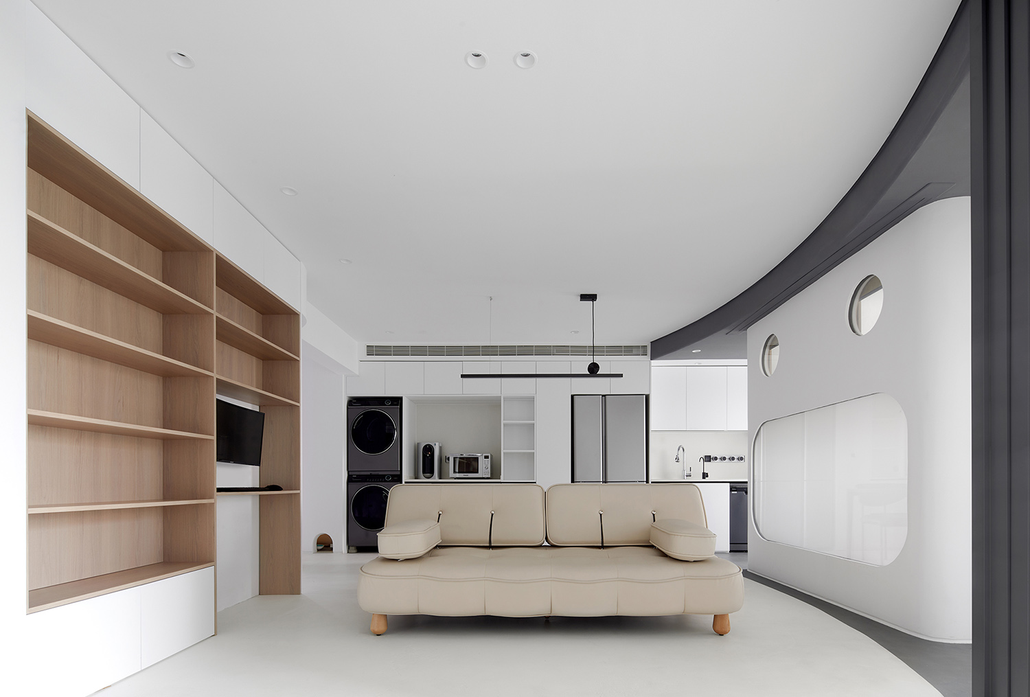 Small warm minimalist living area with compact seating, wood tones, and open floor space.
