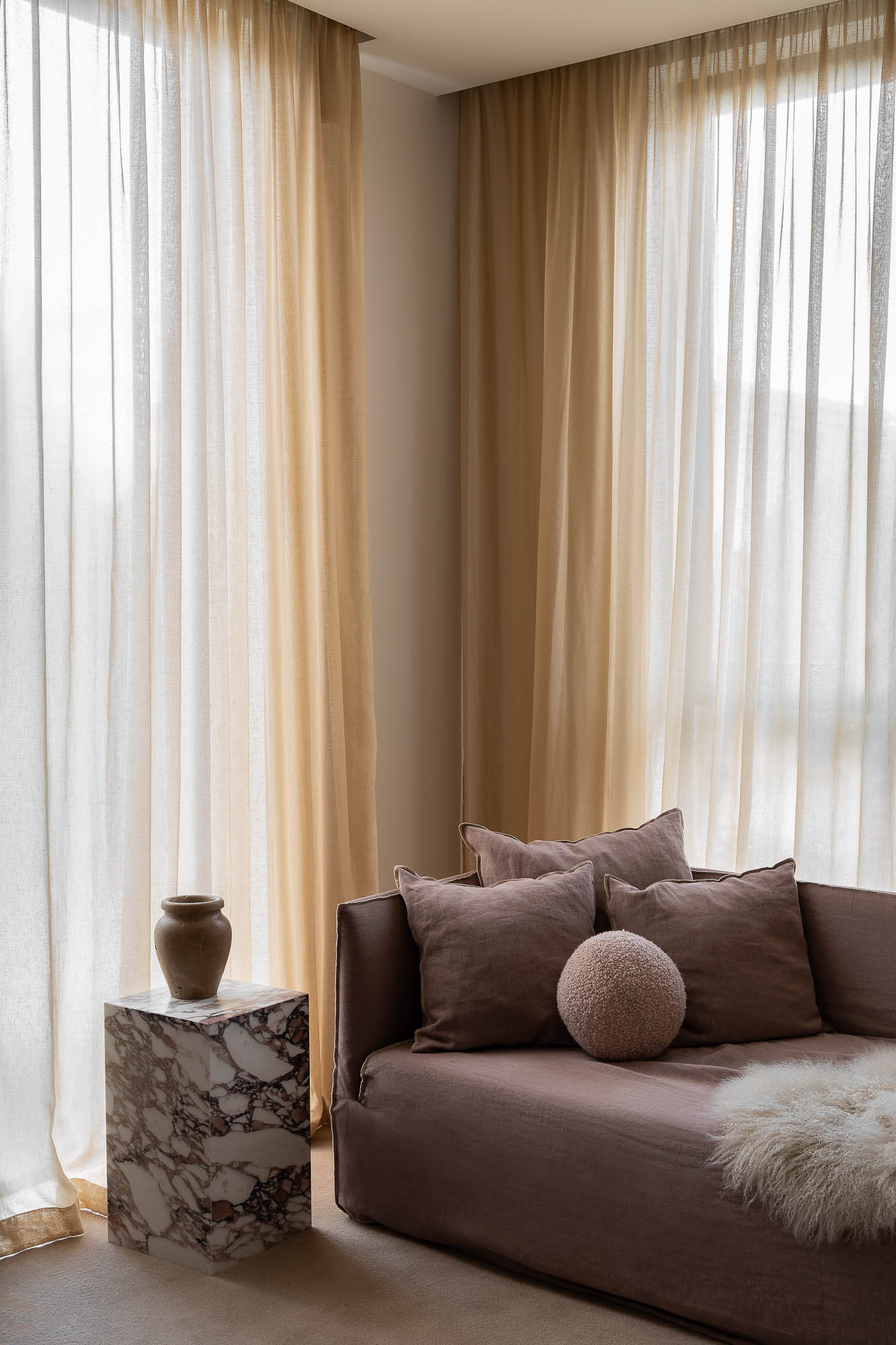 Minimalist living room with curtains, marble side table, warm neutral tones, and soft filtered light.