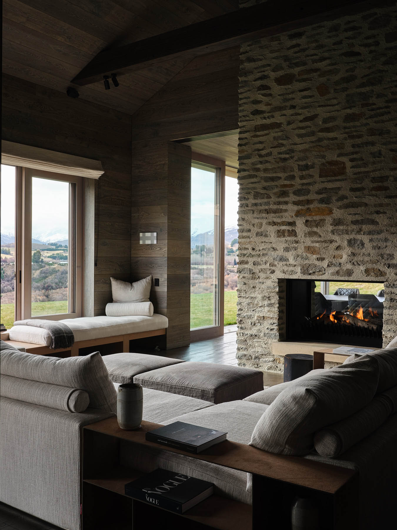 Modern living room with a stone fireplace flanked by warm wood-clad walls serving as a dramatic focal divider.