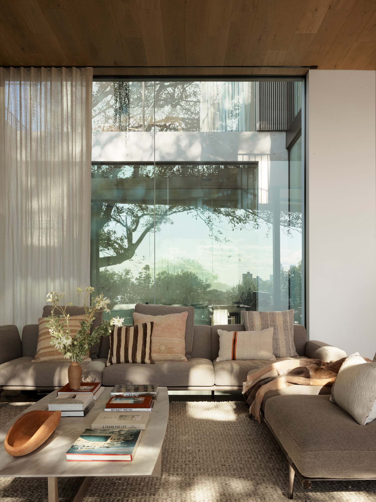 Modern living room with glass surfaces, fabric seating, and afternoon light reflecting through the window.