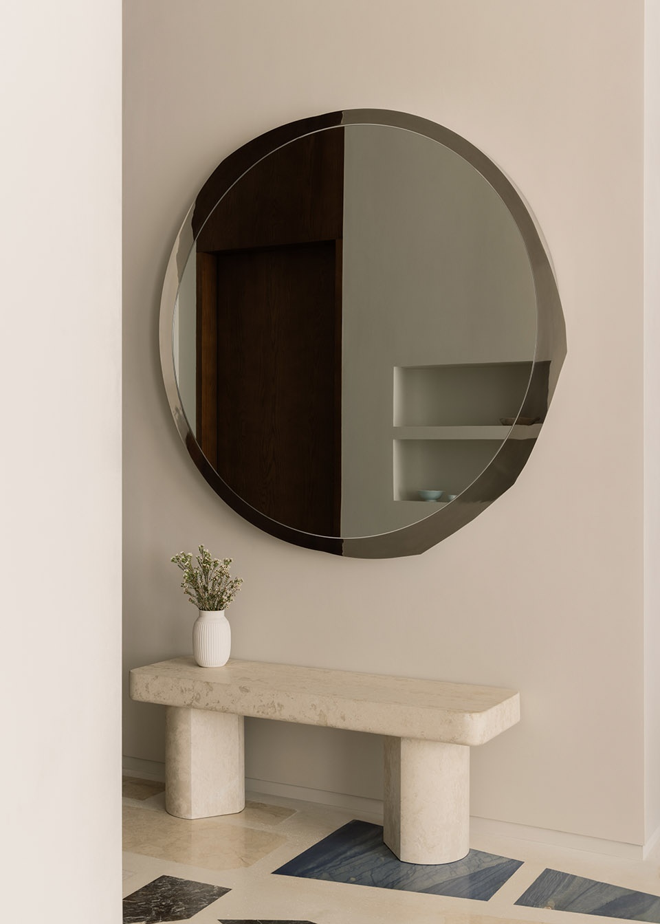 Small narrow entryway in warm neutral tones with a slim stone bench and console styling.