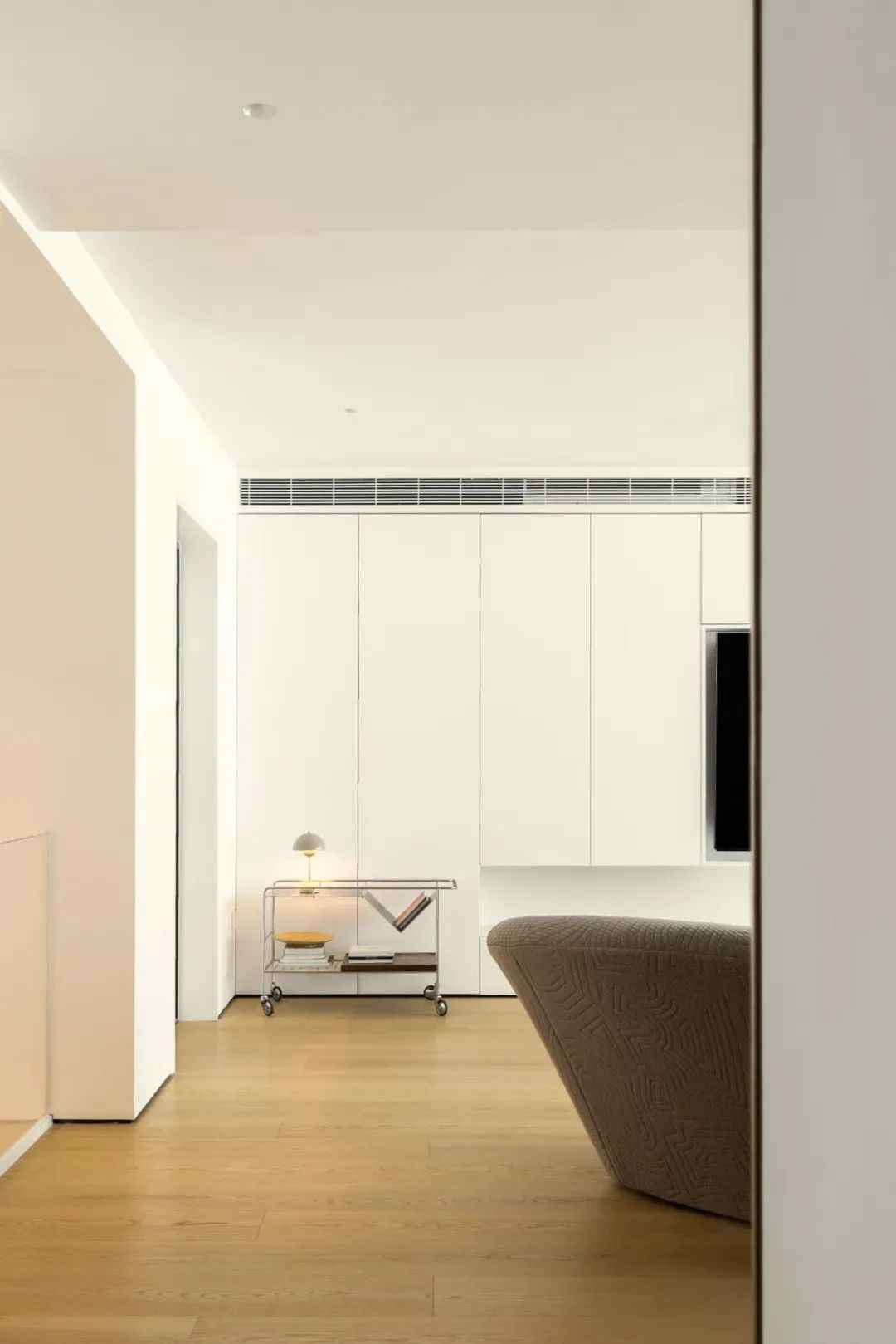 Modern minimalist living room with pale wood flooring, white walls, and streamlined built-in storage.