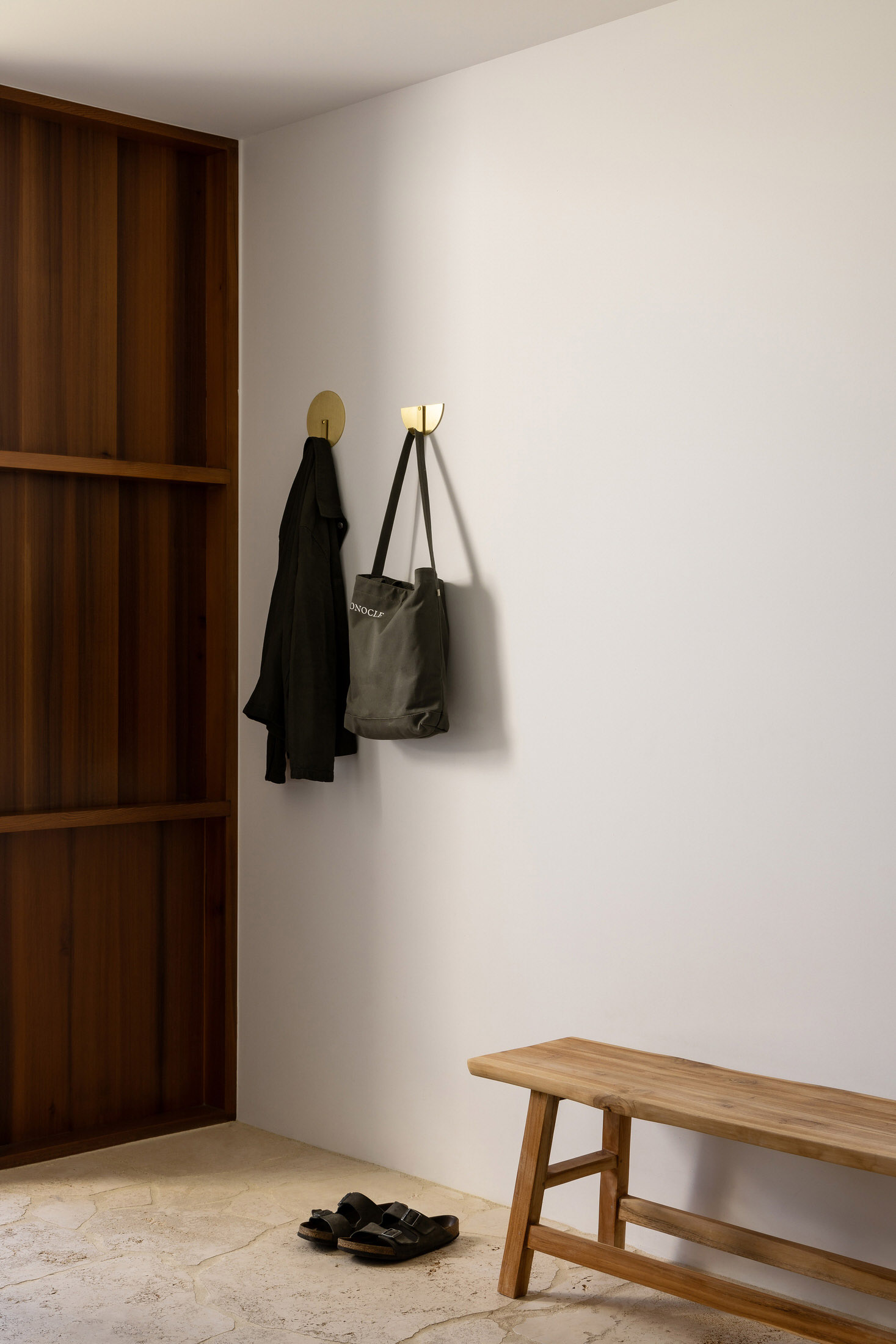 Small modern entryway with wood finishes, metal wall hooks, and narrow freestanding storage.