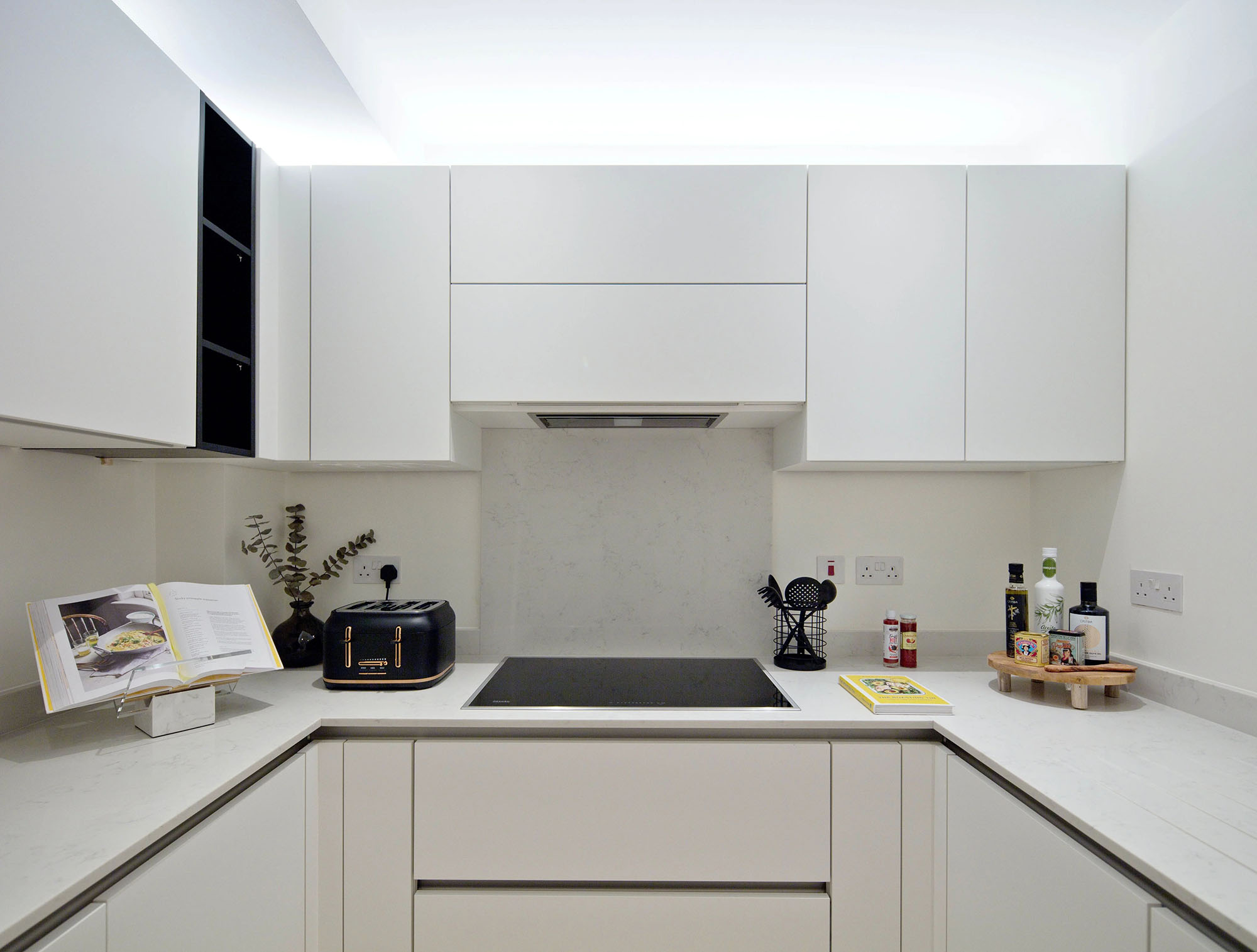 Minimalist kitchen with bright white cabinets and warm overhead lighting — showing the impact of a well-layered 2700K lighting scheme in a narrow kitchen