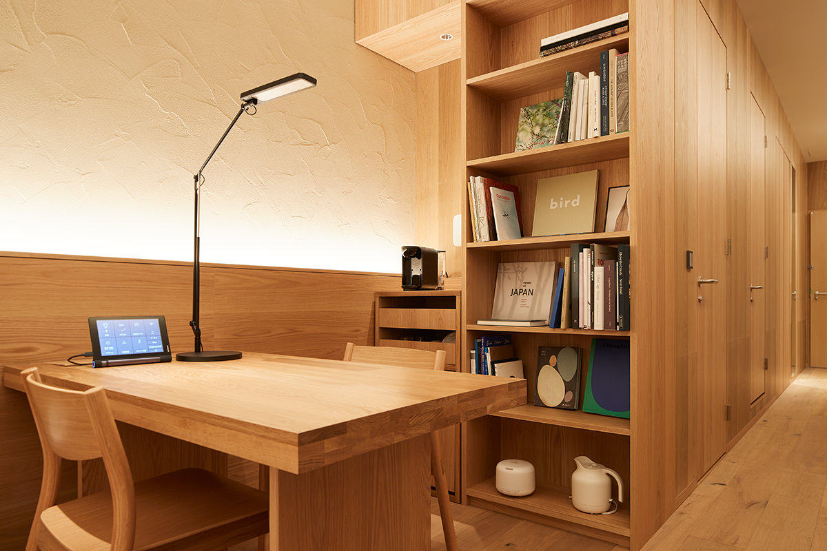 Floating wood desk with open wall shelves in a small minimalist home workspace lit by natural light.