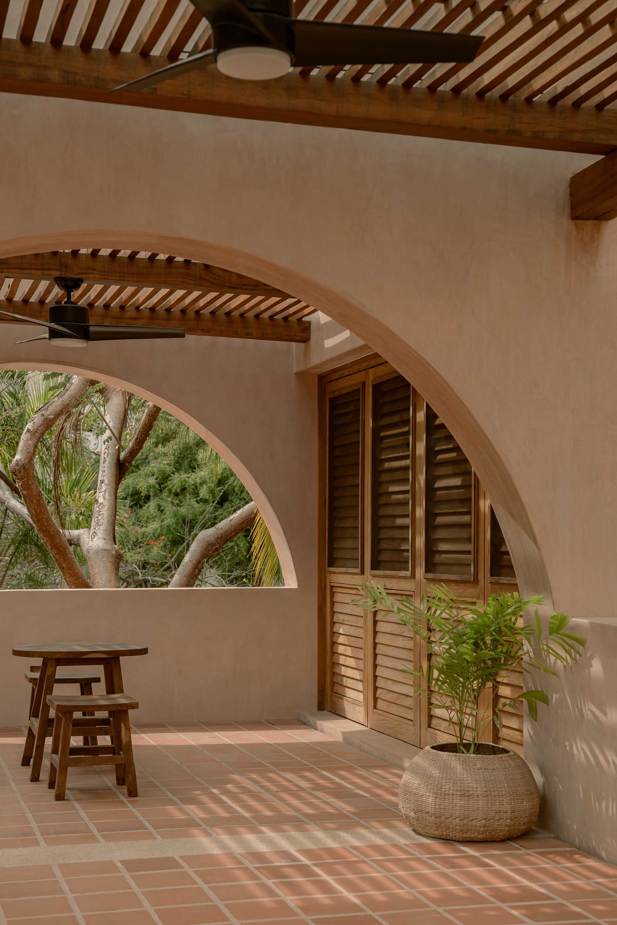 Minimalist Mediterranean porch with terracotta tones and shaded outdoor seating near a summer facade.