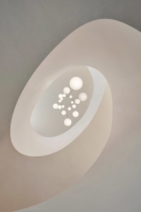 Minimalist ceiling fixture with spherical lights arranged in a flower-like pattern, featuring a light-colored, smooth, curved