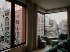 Modern living room with cityscape view through large windows, featuring soft textiles and upholstered seating