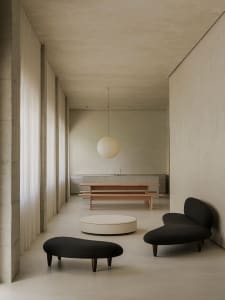 A modern living room with concrete walls, minimalist furniture, and a round ottoman.