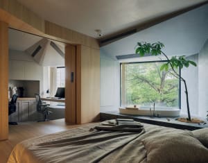A minimalist bedroom with wood floors, a wooden bed frame, and a large window overlooking greenery.