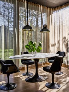 A dining room with black furniture, a round table, and green foliage in a vase.