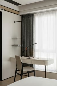 A minimalist bedroom workspace with a white desk and chair, a modern lamp, and a window with gray curtains.