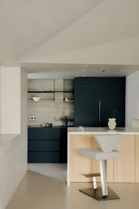 A modern minimalist kitchen featuring black cabinetry and a concrete backsplash.