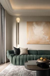 Modern minimalist living room with a green velvet sofa, abstract painting, and black coffee table.