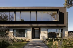 A modern residential building featuring large glass windows and wooden materials.