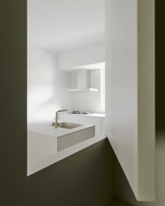 A modern kitchen with white countertops and walls, featuring a stainless steel faucet and a gas stove.