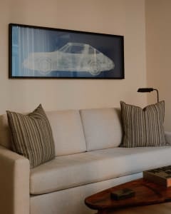 A comfortable living room with a beige couch, black and brown striped throw pillows, a dark wooden table, and a framed x-ray 