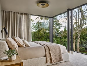 Contemporary bedroom featuring textured furniture and large windows overlooking greenery.