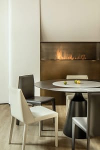 Modern dining room featuring a metallic bronze and leather table, chairs, and fireplace.