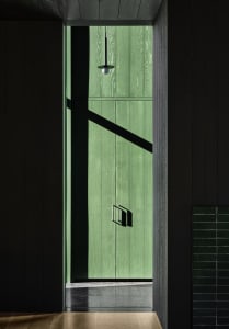 A modern green wooden doorway with sunlight casting a shadow