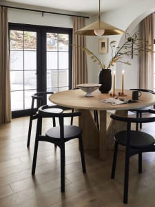 A modern minimalist dining room with a wooden table, black chairs, and a large pendant light.