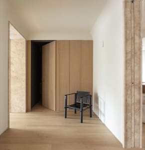 Modern minimalist interior with oak wood flooring, walls, and wardrobe, featuring a black chair.