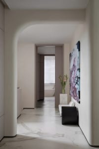 Modern interior corridor with marble flooring leading to a bathroom with a bathtub.