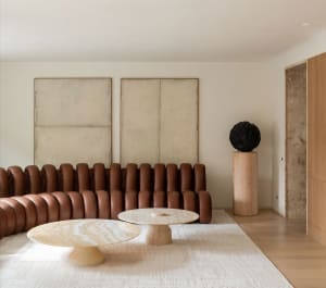 Modern, industrial-style living room with a unique, cushioned leather sofa, round marble tables, and minimalist artwork on th
