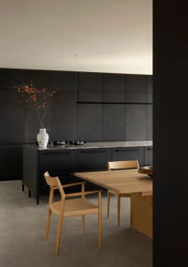 A modern kitchen with black panels and a wooden dining table.