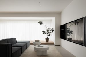 A modern minimalist living room with a black sectional sofa, white coffee tables, a large potted plant, and floor-to-ceiling 