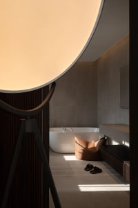 Modern bathroom with a white freestanding tub, brown ceramic tiles, and a large light fixture