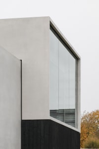Modern architectural exterior featuring concrete and black wooden panels with a large glass window.