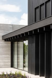 Modern building exterior with concrete and wooden panels, featuring glass windows and a minimalist design.