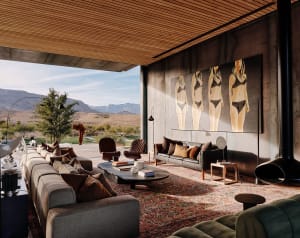 A modern living room with a concrete and wood interior design, featuring large windows and a floor-to-ceiling fireplace.