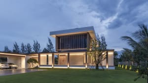A modern residential exterior with glass, concrete, and wood materials at dusk.