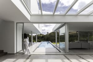 A modern residential interior with a sleek, minimalist design featuring a concrete floor, large windows, and a view of a swim