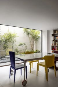 Contemporary dining room with glass table, yellow chairs, and indoor garden.