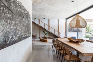 Modern dining room with industrial design, featuring concrete walls, a wooden dining table, and a decorative wall hanging.
