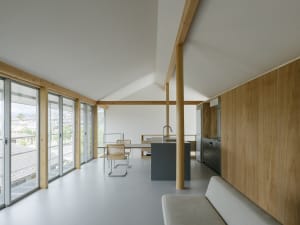 A contemporary living room with wooden accents and clean lines, featuring a sofa, table, and large windows.