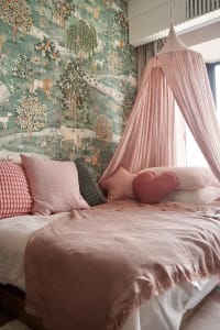 Bedroom with pastel-colored textiles, a canopy, and whimsical wallpaper featuring animals and trees.