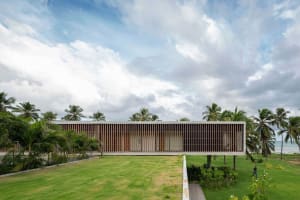 Modern architectural exterior with wooden and concrete materials, set against a cloudy sky and surrounded by greenery.