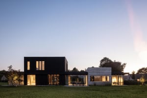 Large modern residential house with black and white exterior, featuring glass windows and a large yard.