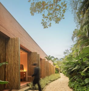 A modern residential exterior featuring bamboo walls and a gravel path surrounded by lush greenery.