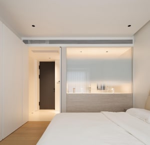 Modern minimalist bedroom with white walls, light hardwood flooring, and a large white bed.