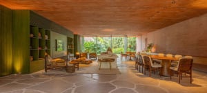 A modern living and dining room featuring concrete flooring and furniture, with greenery outside.
