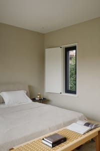 A minimalist bedroom with neutral-toned textiles and a window showing greenery outside.