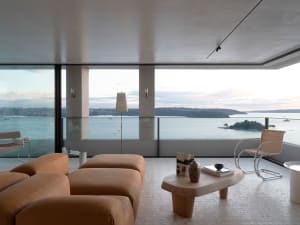 A modern living room with leather furniture, glass walls, and a view of the ocean.