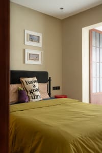 A minimalist bedroom with a green bedspread and a pillow that says 'have a good time'.
